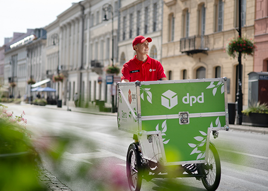 Kurier DPD na rowerze cargo z logo firmy na tle miejskiej ulicy.